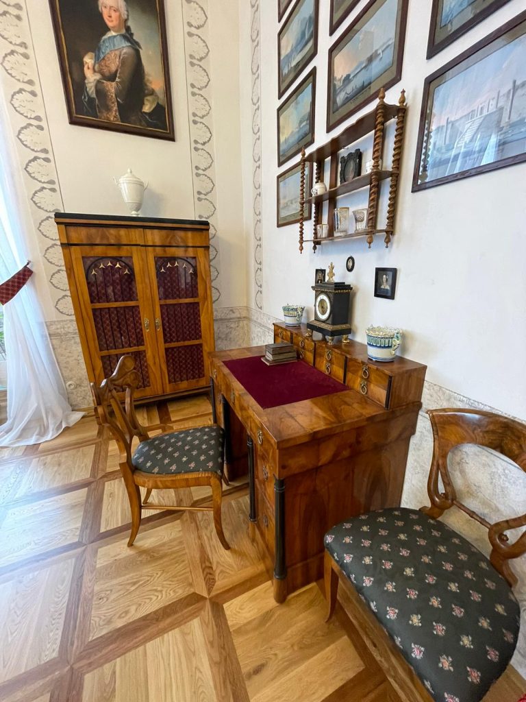 Historická kancelář na zámku v Litomyšli s dřevěným nábytkem a obrazy.