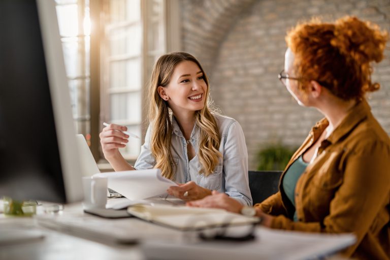 Young happy businesswomen communicating while working in the off