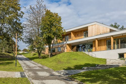 Moderní budova Domu pro Julii v Brně obklopená zelení a stromy, pohled z přístupové cesty.