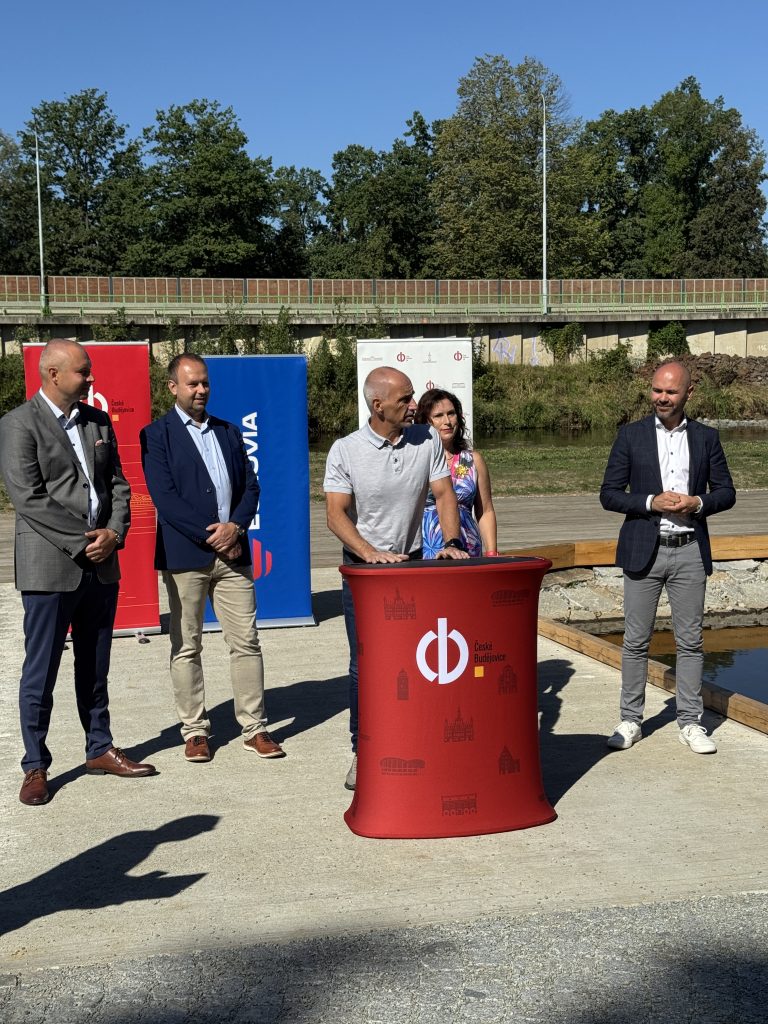 Zástupci města a partnerů při slavnostním otevření Slunečních ostrovů, u řečnického pultu s logem města a propagačními bannery.