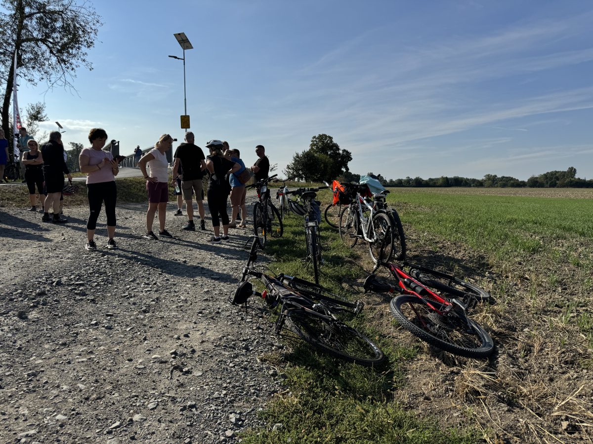 Skupina cyklistů stojí na štěrkové cestě uprostřed polí.