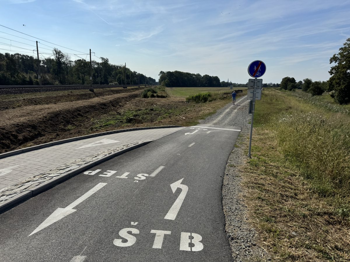 Cyklostezka s mostem přes trať, po cestě jede cyklista.