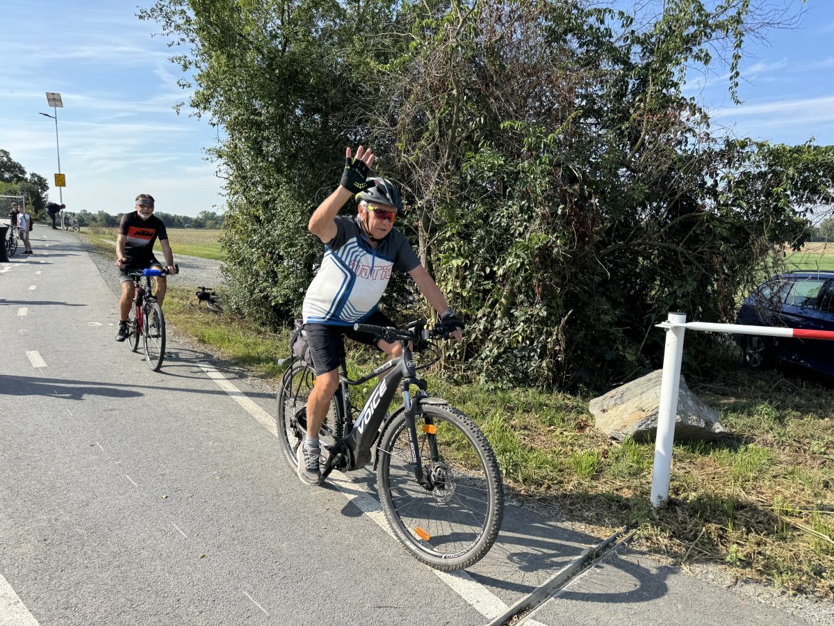 Starší cyklista na kole mává do objektivu při jízdě po nové stezce.