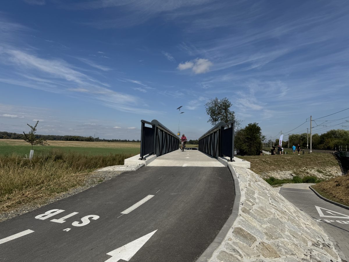Cyklostezka s mostem přes trať, po cestě jede cyklista.
