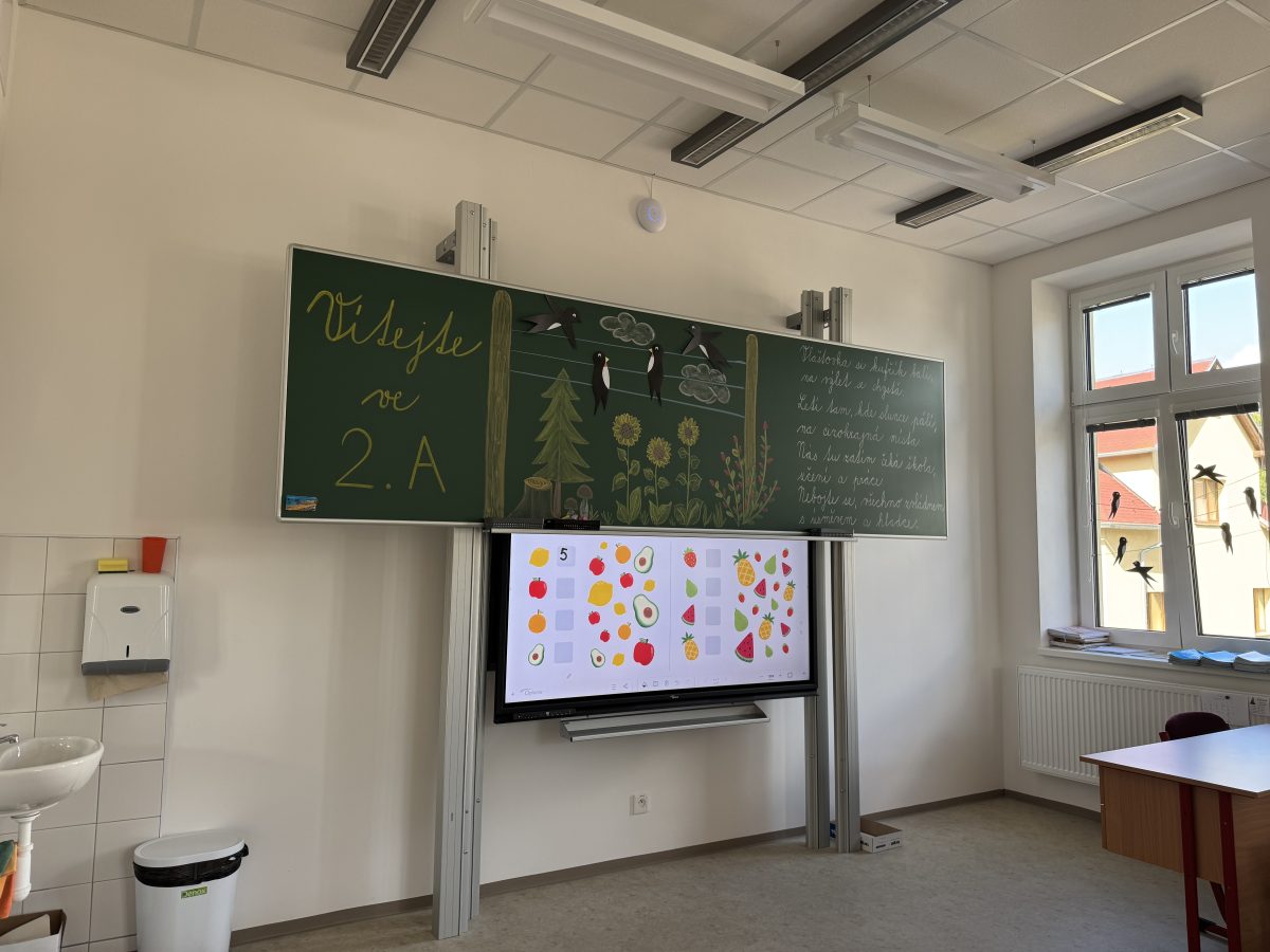 Třída se zelenou tabulí a interaktivní obrazovkou v základní škole v Chrastavě.
