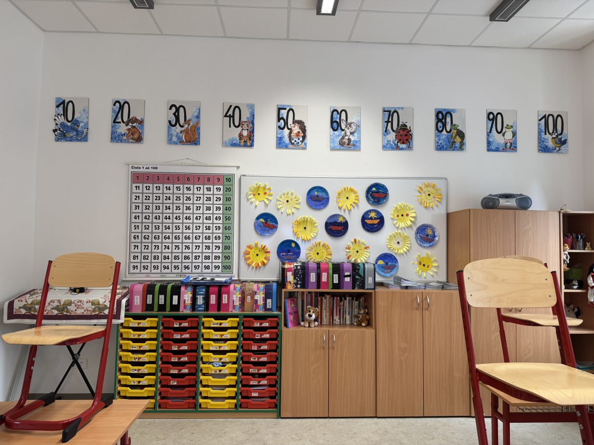 Učebna s barevnými boxy, výukovými čísly do sta a dětskými výtvarnými pracemi.