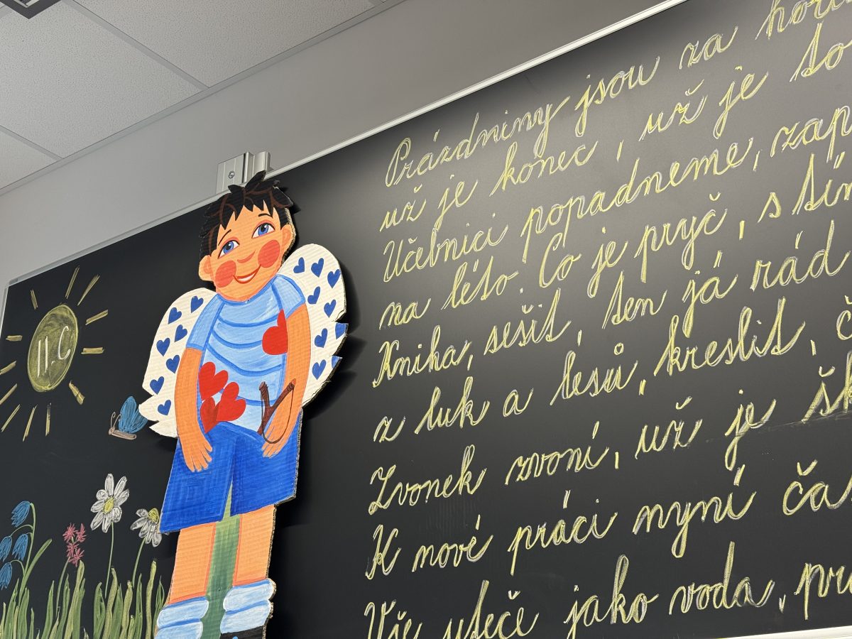 Černá tabule s psanou básní a dětskou výzdobou v podobě postavičky a květin.