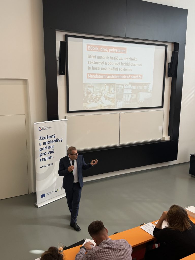 Generální ředitel CRR na konferenci Architektonická soutěž ve Zlíně prezentuje před plátnem s výrazným červeným nápisem.