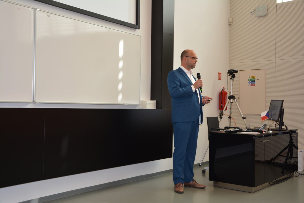 Řečník v modrém obleku prezentuje na konferenci Architektonická soutěž ve Zlíně.