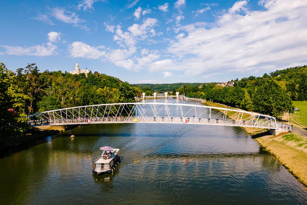 Pohled na lávku přes Vltavu v Hluboké s Hlubockým zámkem na kopci