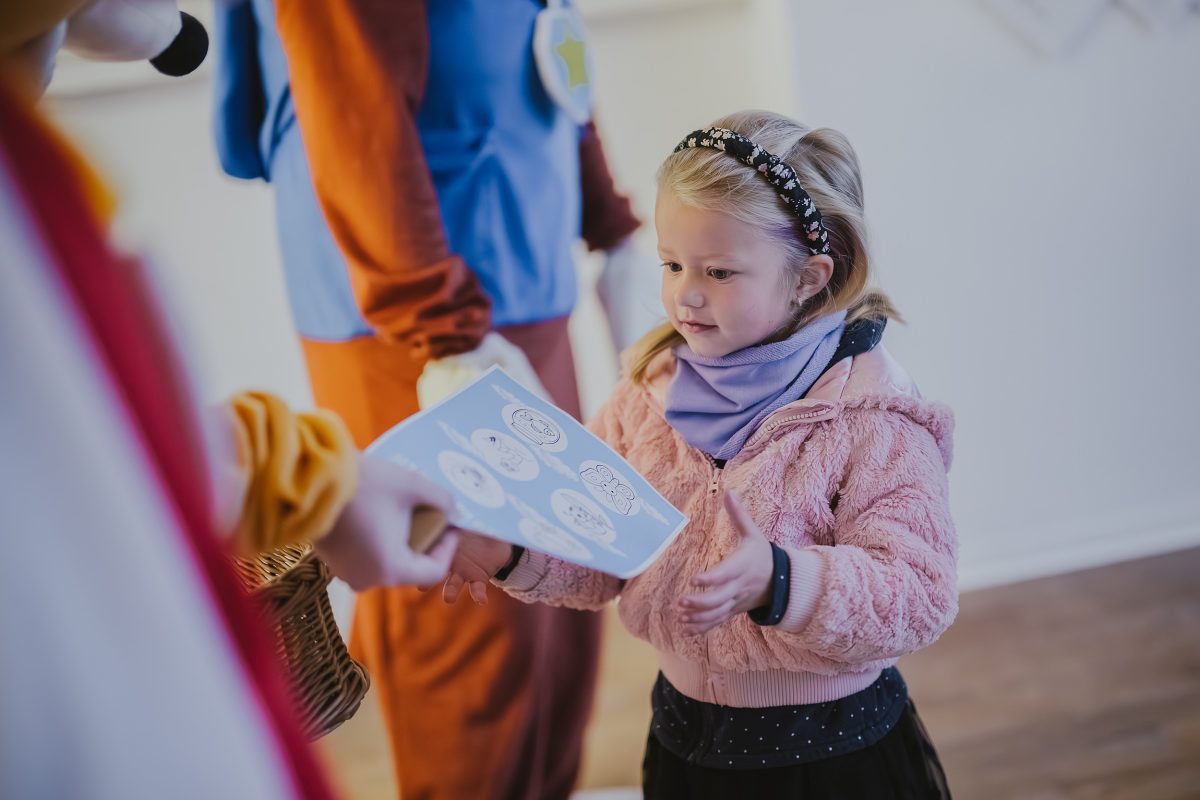 Dívka přebírá omalovánku od maskota při slavnostním otevření školky Zavadilka v Jaroměři.