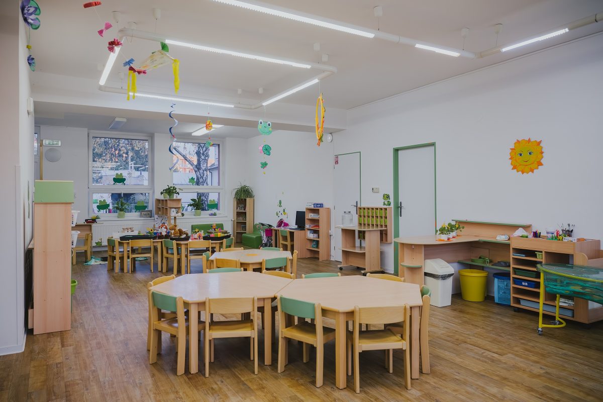 Moderní třída mateřské školy Zavadilka s dřevěnými stoly, židlemi a výzdobou.