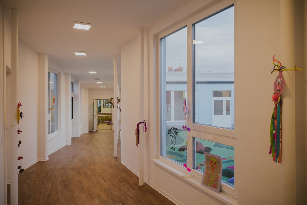 Světlá chodba nové mateřské školy Zavadilka vyzdobená dětskými obrázky.