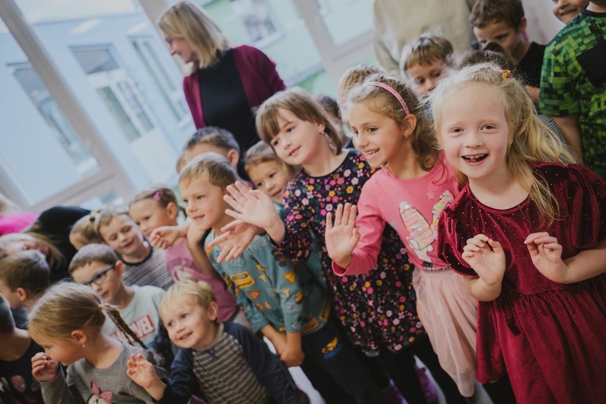 Skupina dětí v nové mateřské škole Zavadilka se směje a mává při slavnostním otevření.