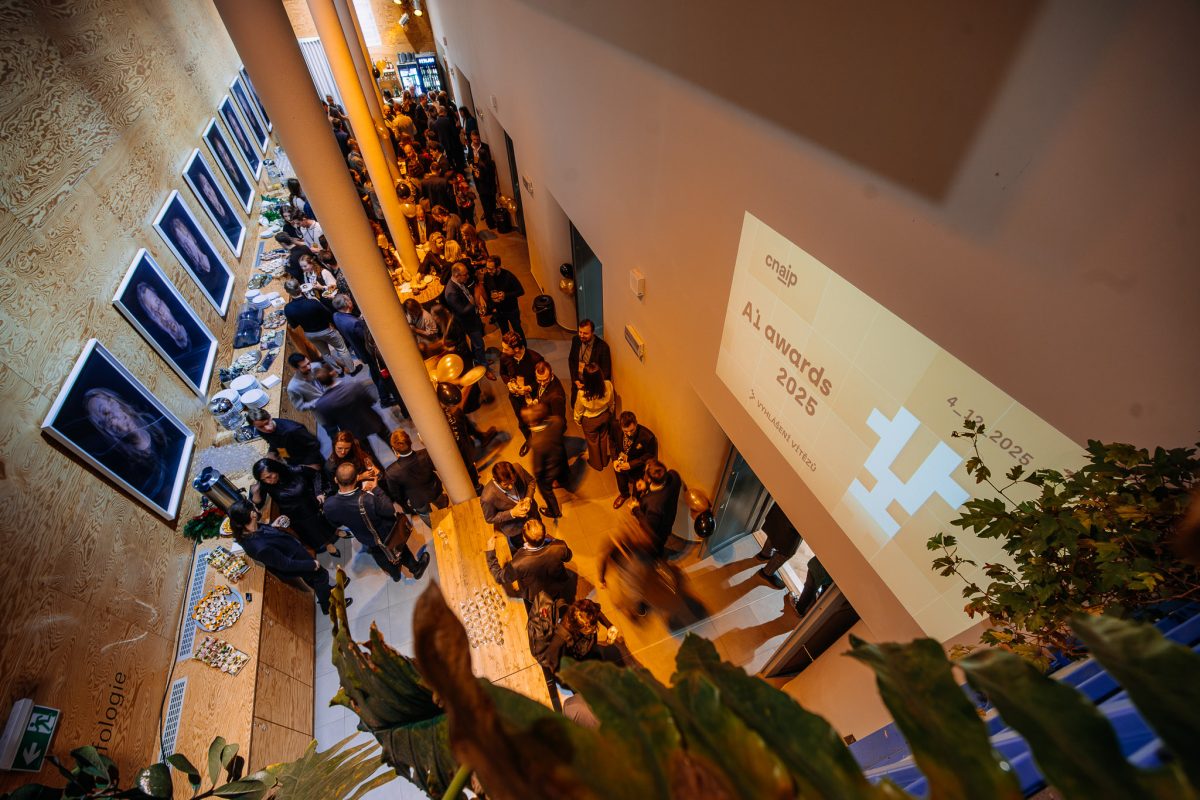 Atmosféra ve foyer během AI Awards 2025, kde se hosté setkávají, povídají si a sledují projekci s logem akce.