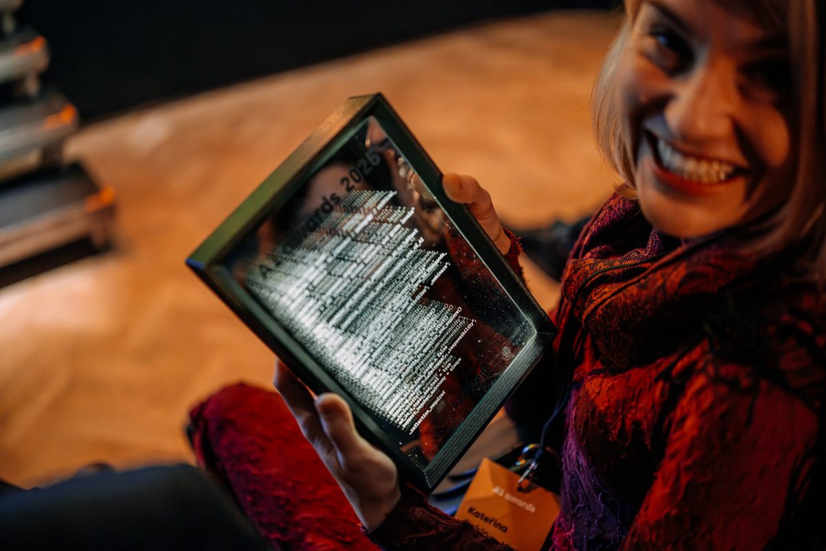Výherkyně AI Awards 2025 drží v rukou skleněnou plaketu s textem ocenění a usmívá se do fotoaparátu.