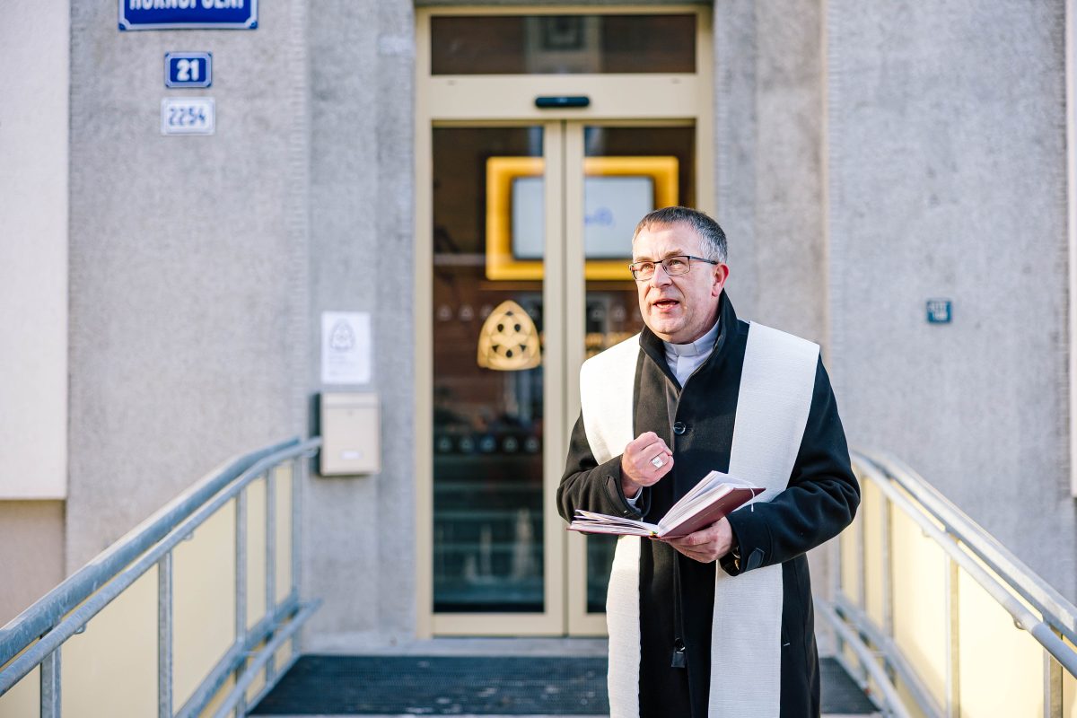 Kněz s knihou promlouvá před vstupem do budovy při slavnostním setkání.