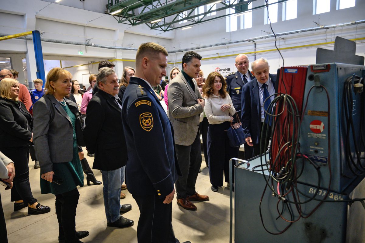 Návštěvníci si prohlížejí vybavení dílny, v popředí stojí svářecí technika.